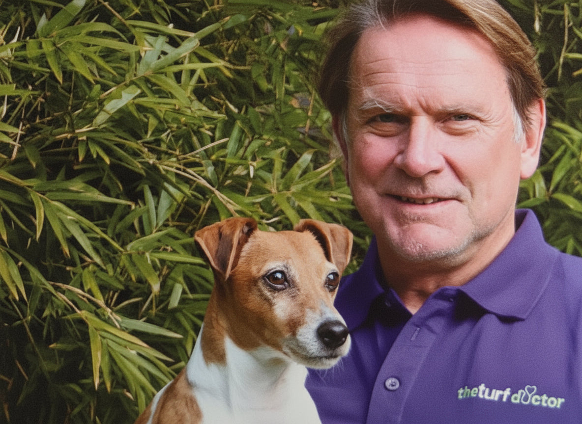 Man in a purple shirt with a dog in front of green foliage